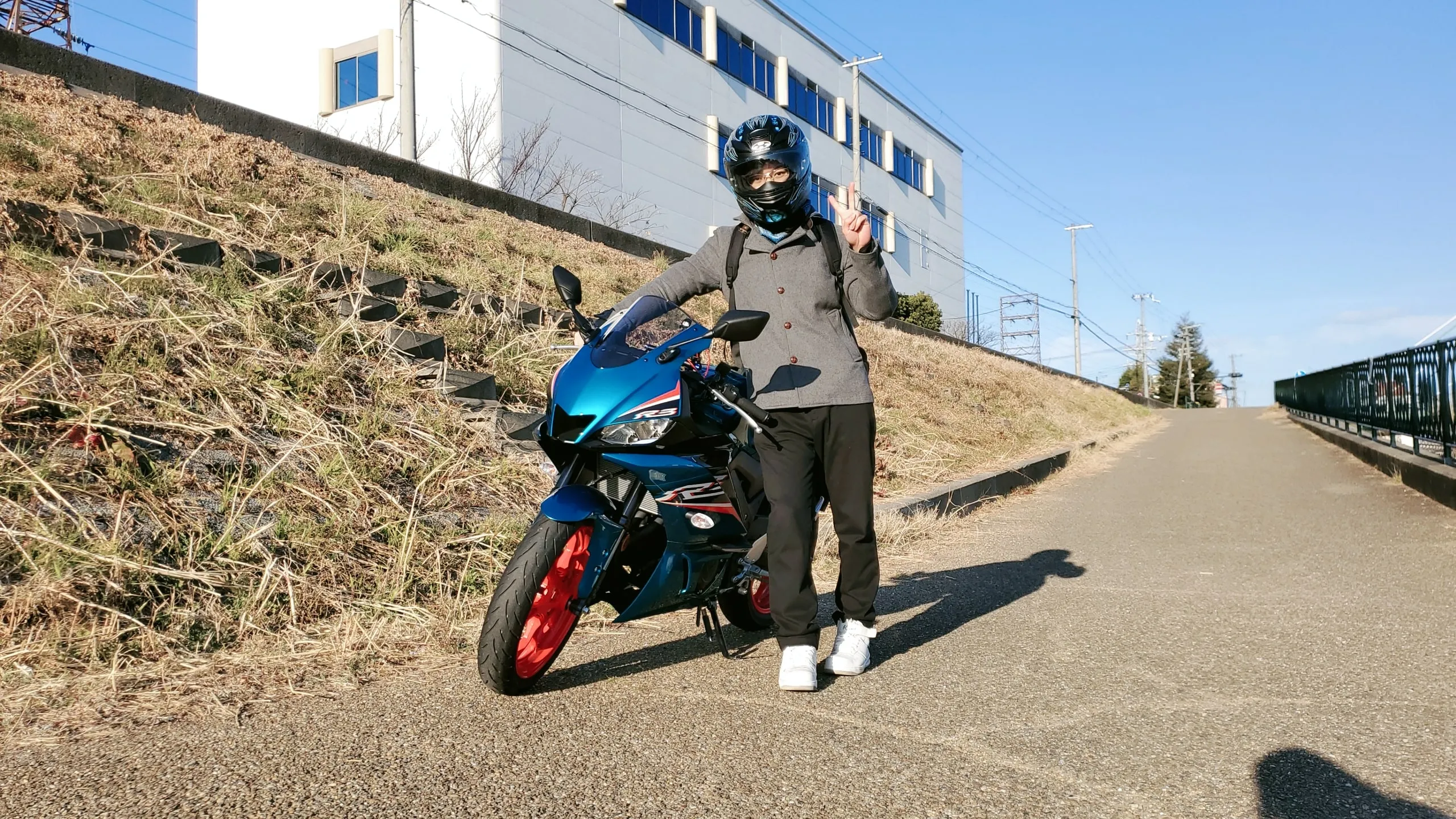 青いバイクのそばでヘルメットをかぶり、ピースサインをするKryιk
